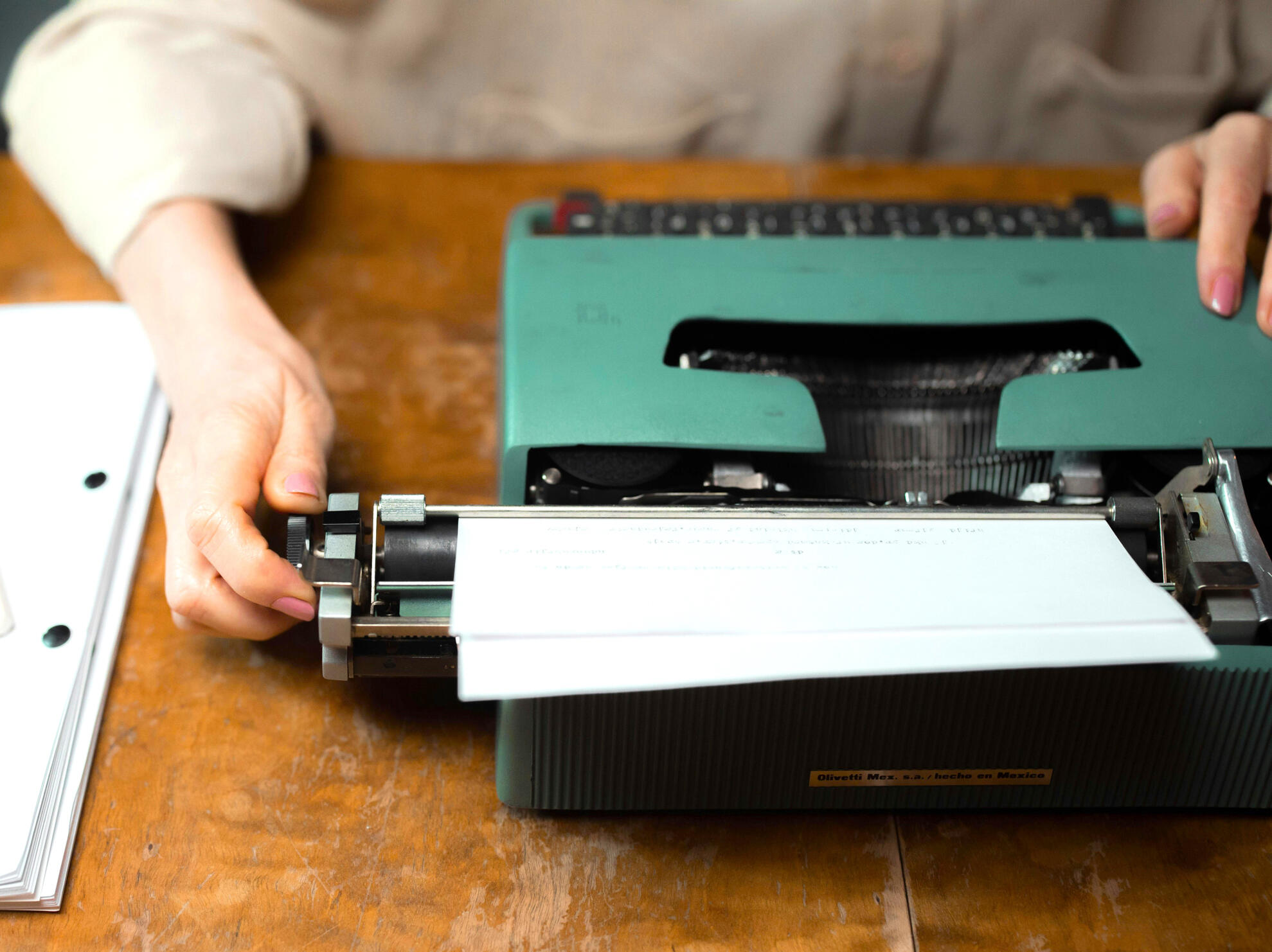 color photo of someone turning the carriage on an old school teal green typewriter image by ron lach via pexels